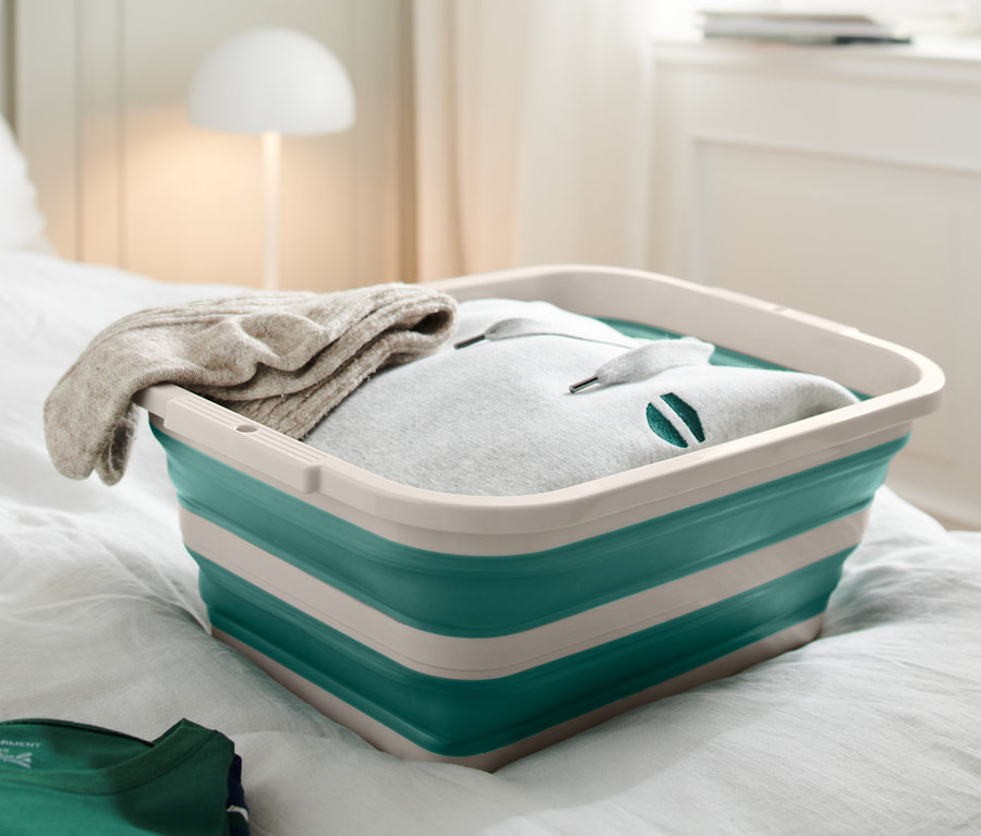 Une bassine à linge et à vaisselle est posée sur un lit avec des vêtements.