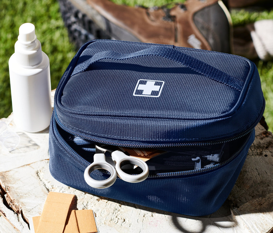 Une trousse à pharmacie bleue avec une croix blanche sur une souche d'arbre à côté d'un spray, des pansements et des chaussures.