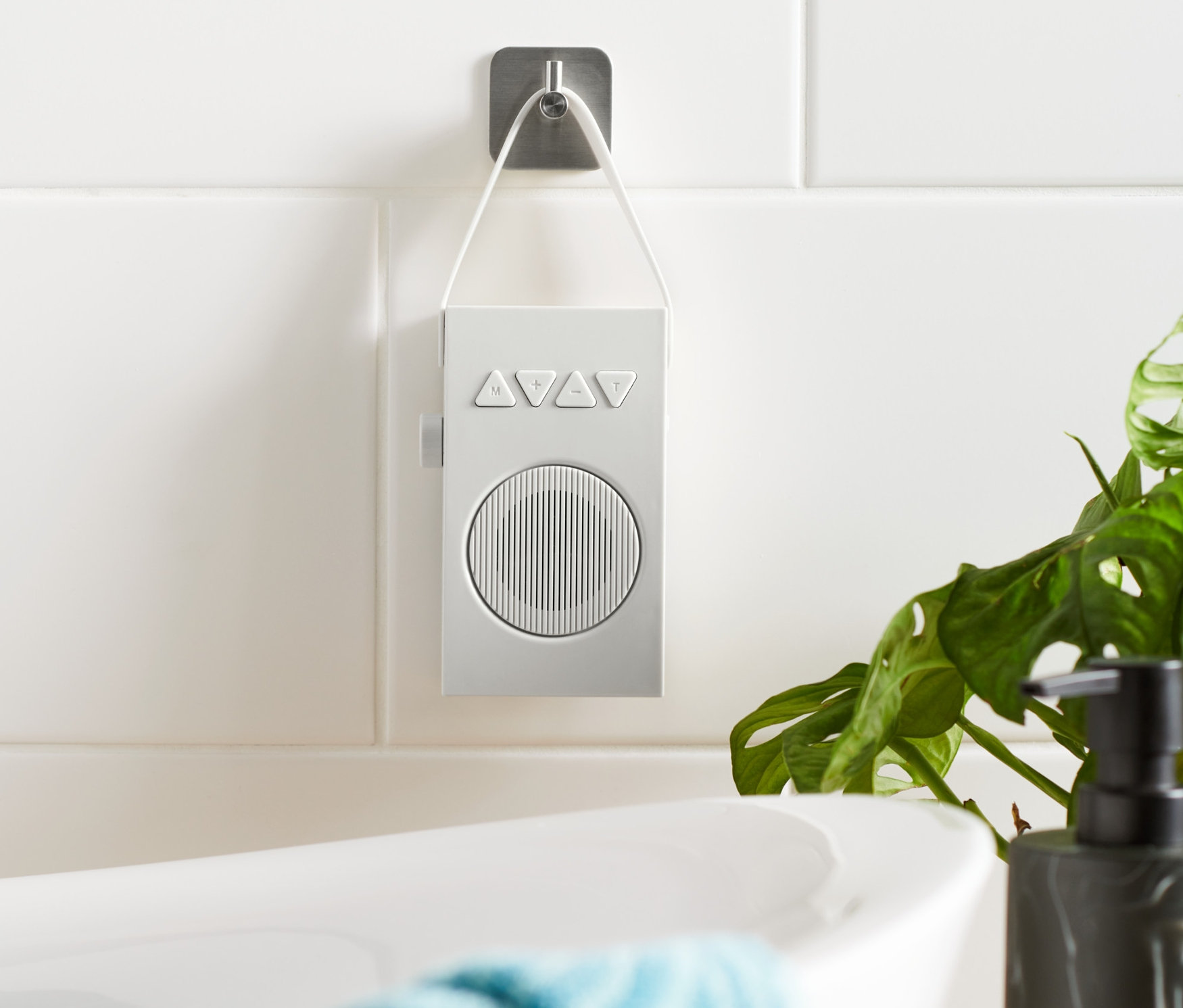 Un radio de salle de bain blanc est accroché à un mur carrelé à côté d'une baignoire.