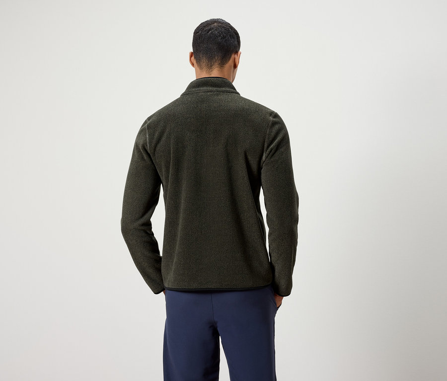 Un homme, dos à la caméra, porte une veste en polaire vert olive et un pantalon bleu marine.