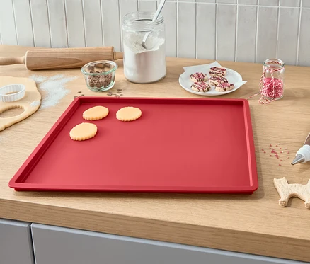 Plaque de cuisson avec pâte étalée, biscuits découpés, glaçage, vermicelles et rouleau à pâtisserie.