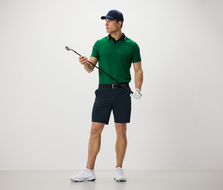 Un homme tient un club de golf et porte un short de sport.