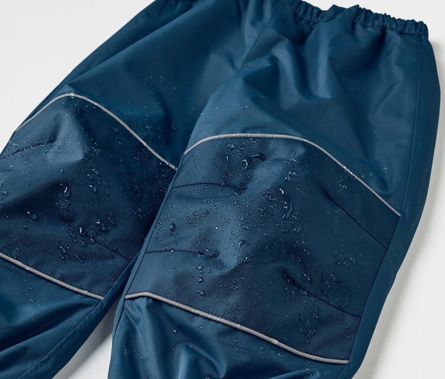 Gros plan sur un pantalon de pluie évolutif pour enfant bleu foncé avec des détails réfléchissants et des gouttes d'eau.