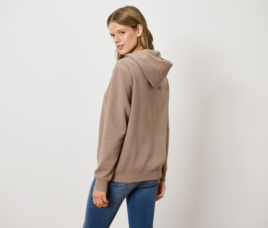 Une femme regardant par-dessus son épaule porte un sweat à capuche marron et un jean bleu.