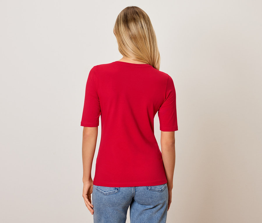 Vue arrière d'une femme aux cheveux blonds portant un t-shirt rouge et un jean bleu.