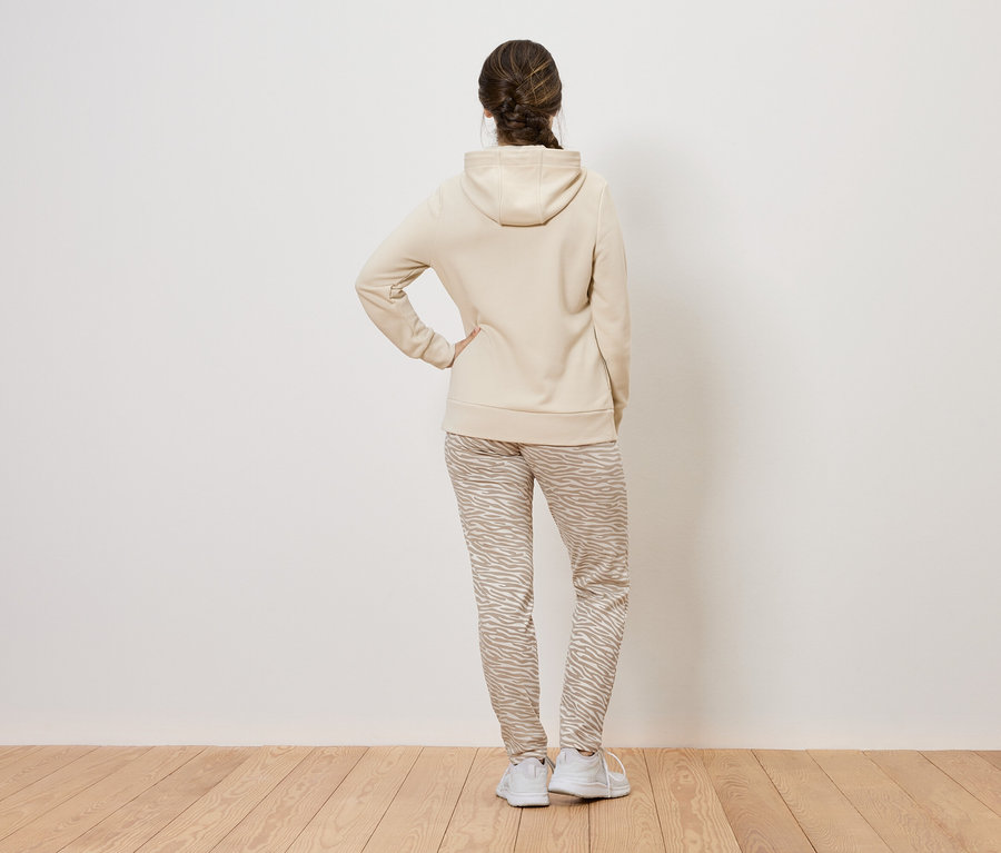 Une femme, vue de dos, porte un sweat à capuche beige et un pantalon à motifs.