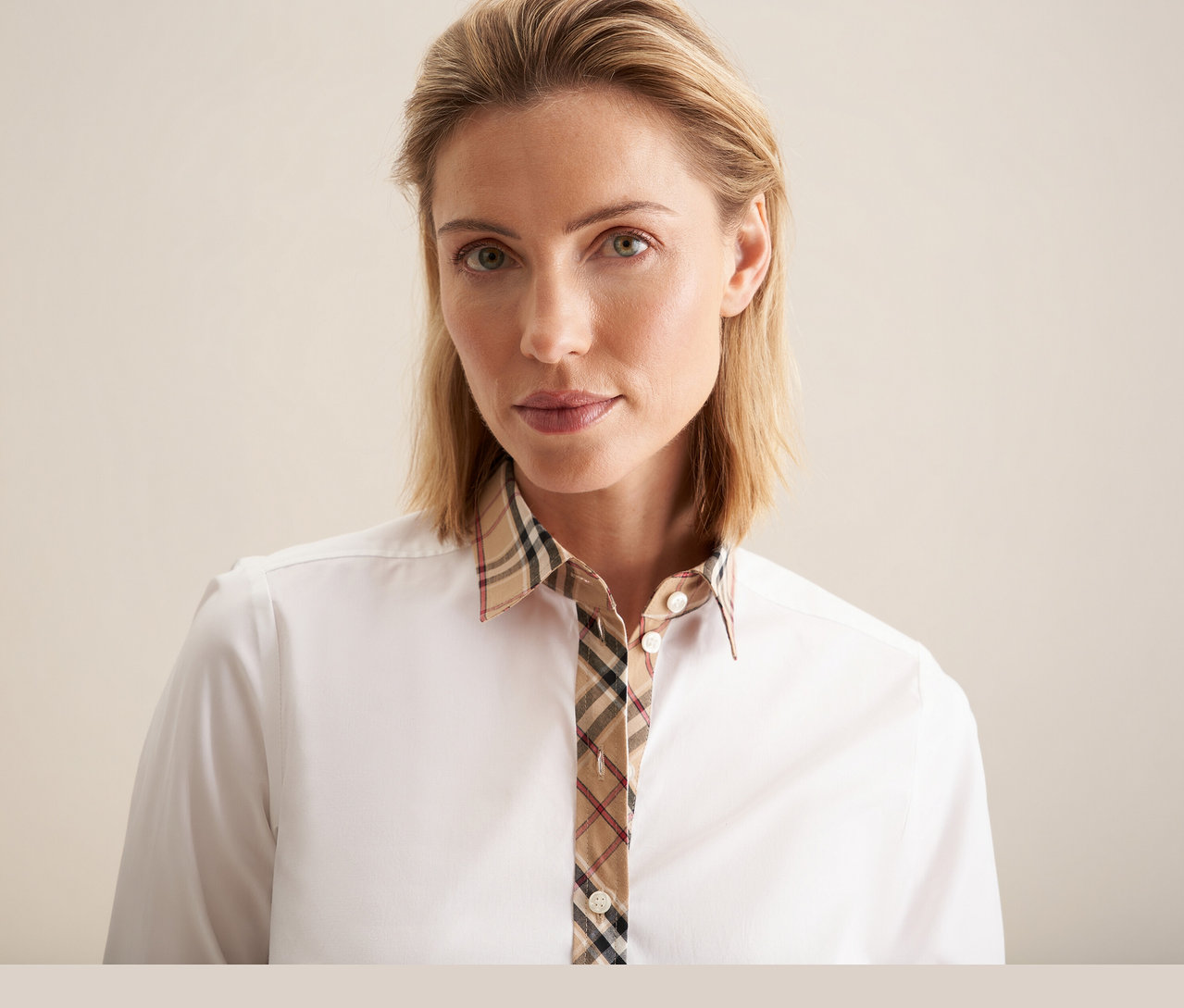 Une femme blonde porte un chemisier en popeline à carreaux Seidensticker blanc avec un motif écossais sur le col et la patte de boutonnage.