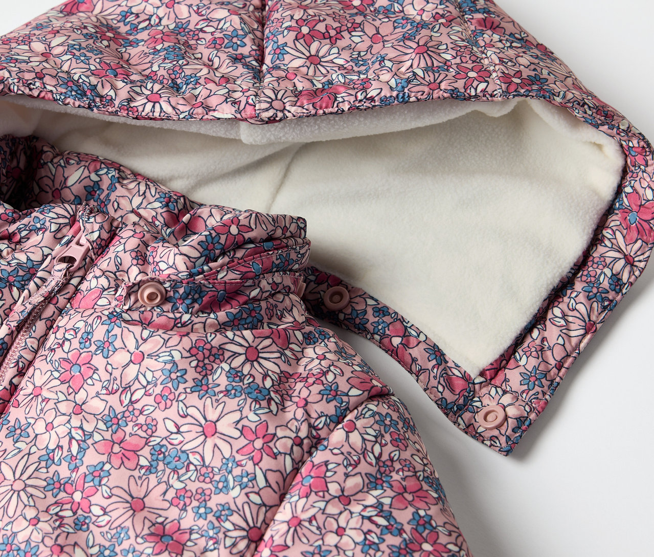 Gros plan sur une combinaison d’hiver pour bébé avec un motif floral et une capuche.