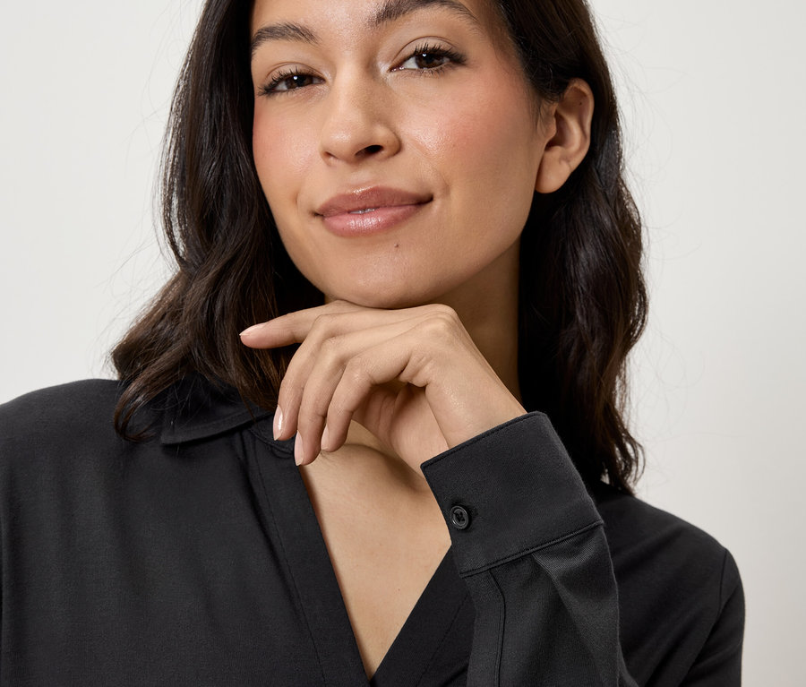 Portrait d'une femme aux cheveux bruns portant une chemise noire et appuyant son menton sur sa main.