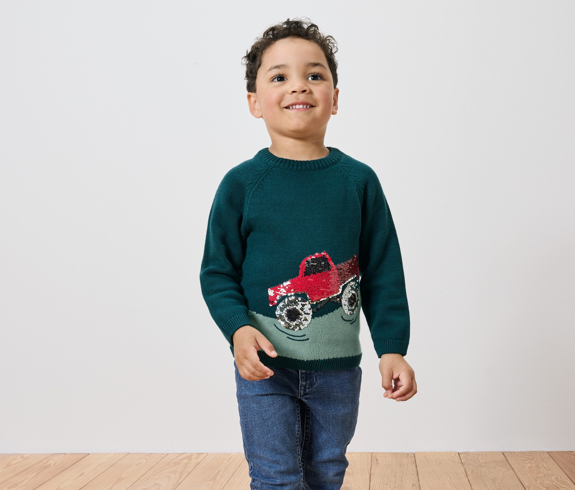 Garçon portant un pull vert avec un camion rouge.
