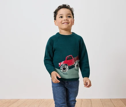 Garçon portant un pull vert avec un camion rouge.