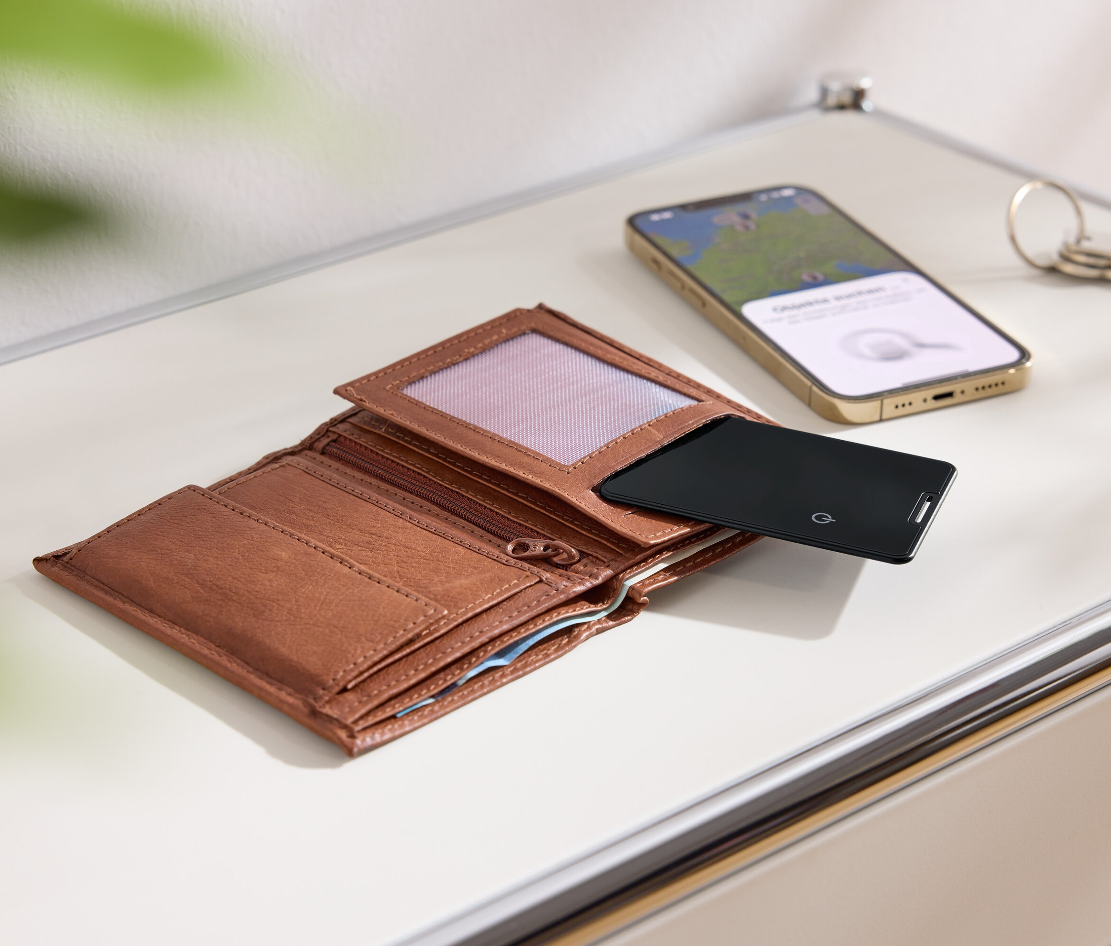 Un portefeuille marron ouvert, une carte noire, un téléphone portable doré et des clés sur une surface blanche.