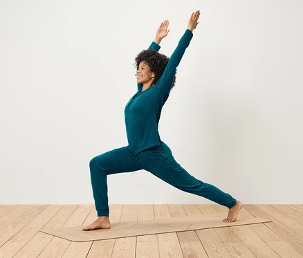 Femme aux cheveux bouclés vêtue d'un ensemble bleu-vert faisant du yoga sur un tapis.