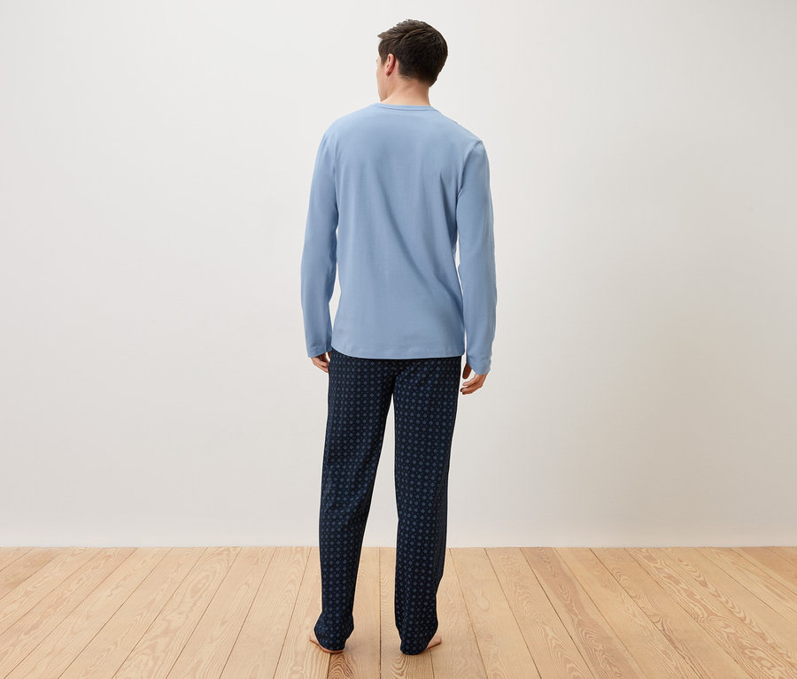 Un homme vu de dos portant un pyjama bleu clair et un pantalon bleu foncé.