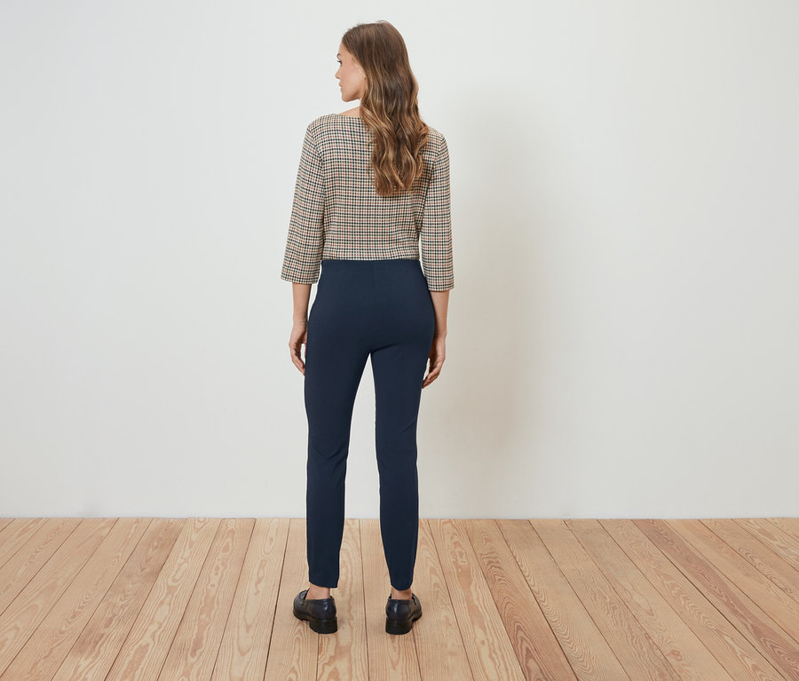 Une femme, vue de dos, porte un chemisier à carreaux et un pantalon bleu marine.