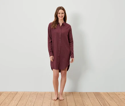 Une femme debout porte une robe chemise rayée bordeaux.