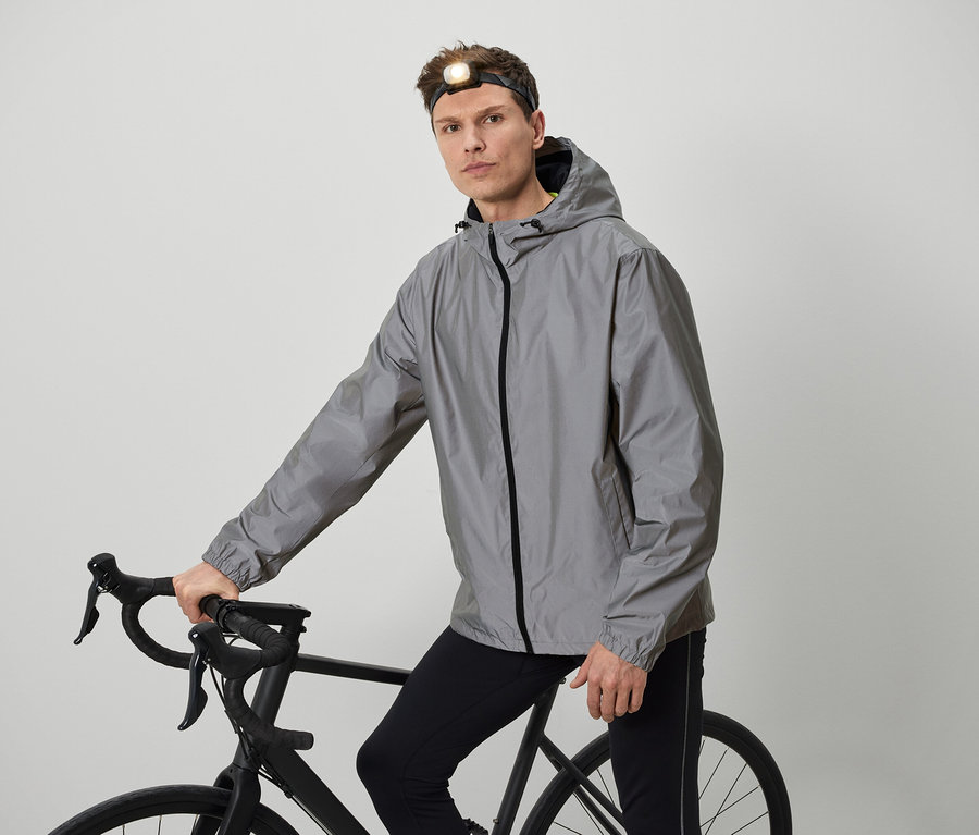 Un homme avec une lampe frontale pose avec un vélo vêtu d'une veste grise.