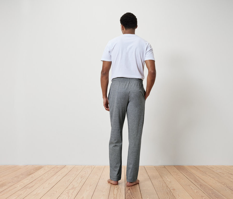 Un homme, vu de dos, porte un t-shirt blanc et un pantalon de survêtement gris.