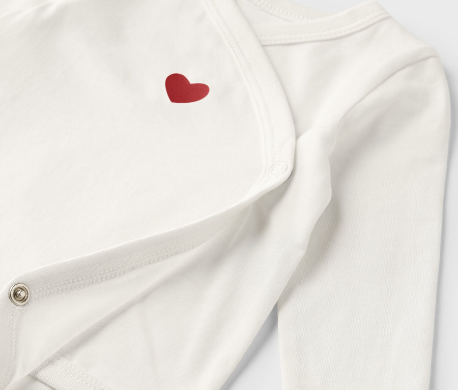 Gros plan sur un body blanc évolutif pour bébé avec un cœur rouge.