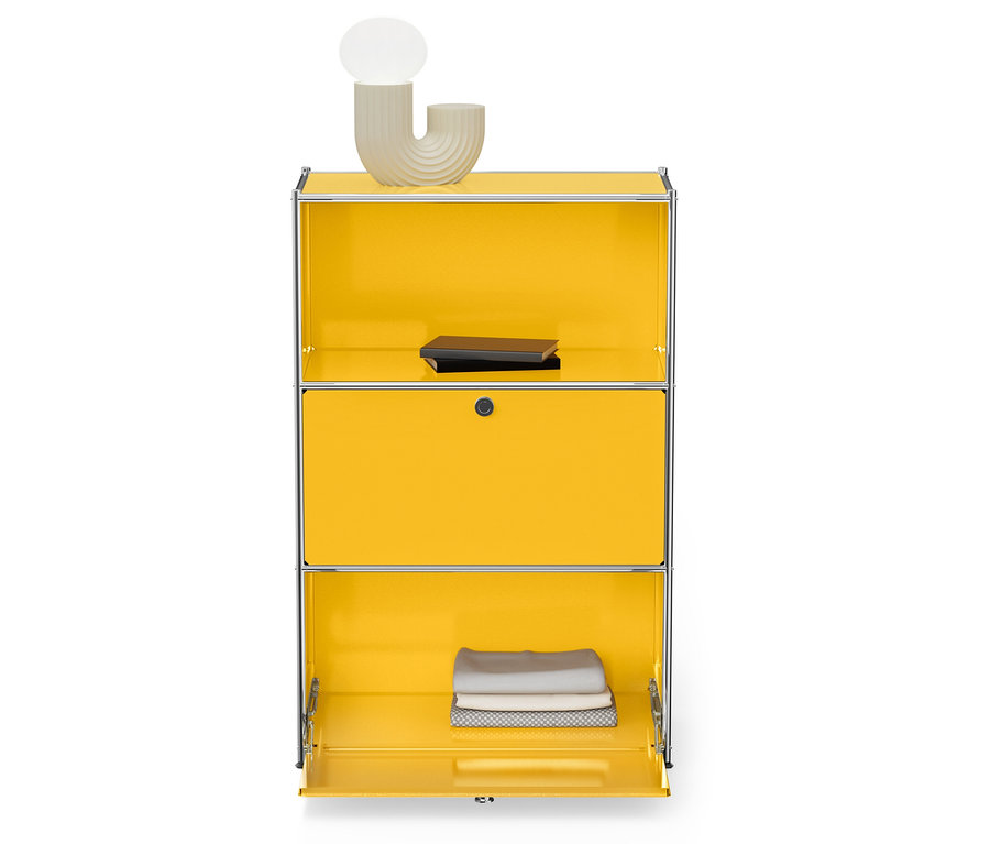 Armoire jaune avec cadre argenté, une lampe et un livre sur le dessus, des serviettes pliées en bas.