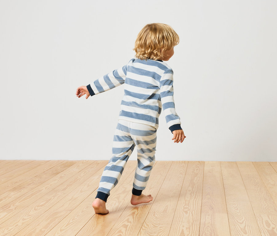 Garçon marchant pieds nus sur un plancher en bois, vêtu d'un pyjama rayé.