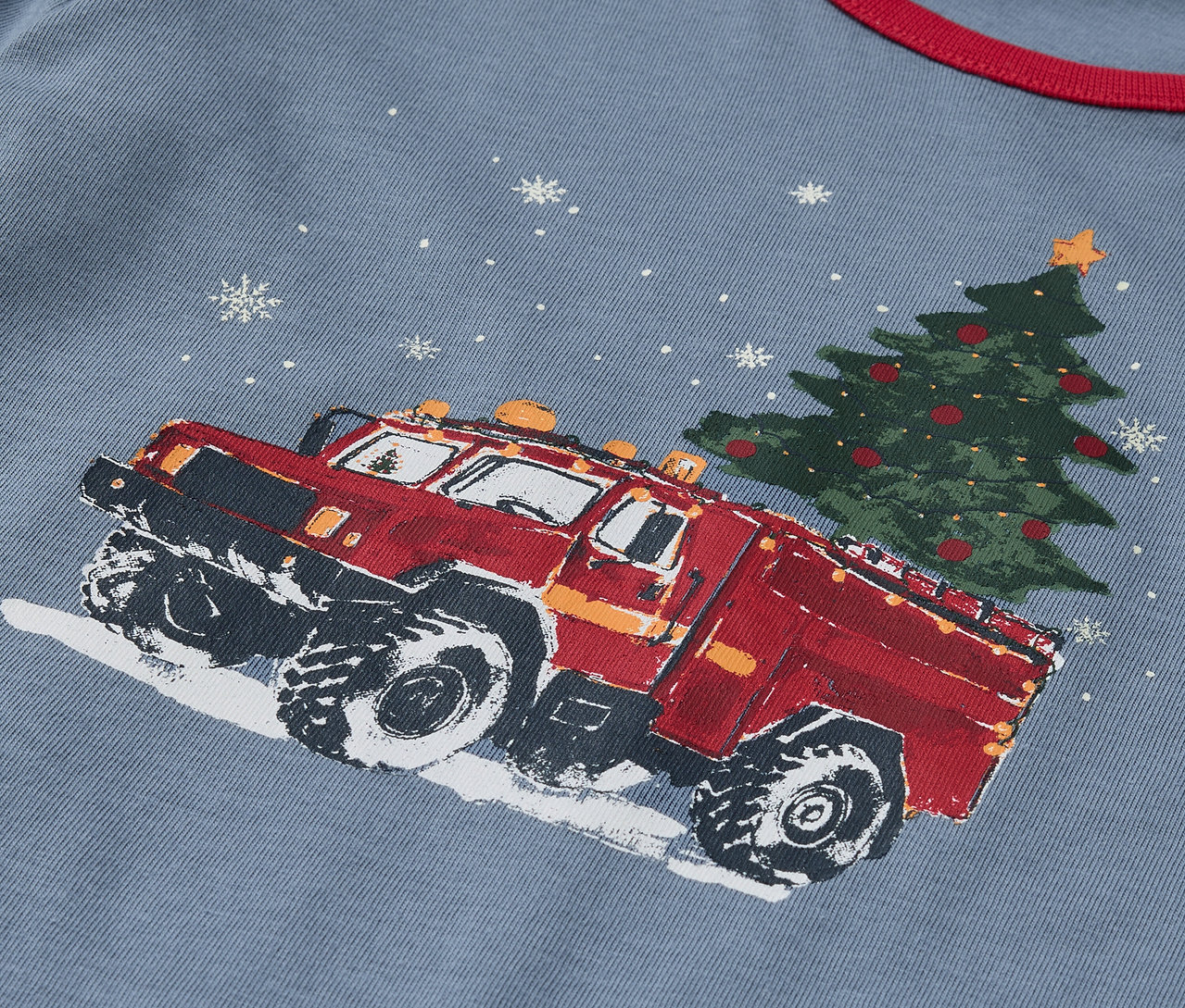 Gros plan sur un t-shirt bleu imprimé d'un camion rouge transportant un arbre de Noël.
