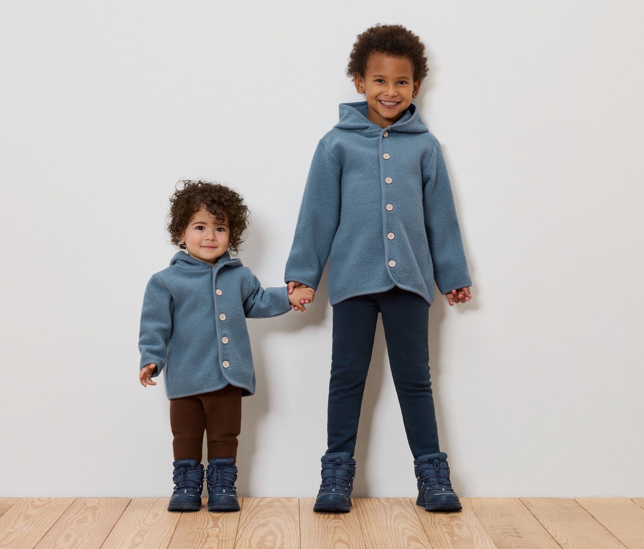Deux enfants se tiennent la main. Ils portent tous les deux des manteaux et des bottes bleues.