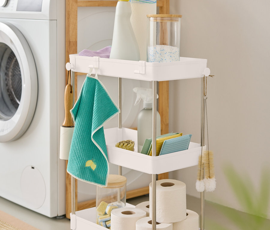 Un chariot blanc à trois niveaux contenant des produits de nettoyage se trouve à côté d'une machine à laver.