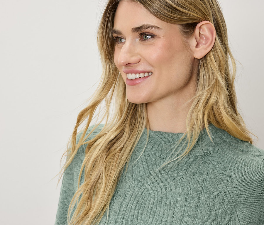 Profil d'une femme souriante aux cheveux blonds portant un pull vert.