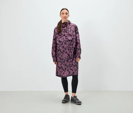 Une femme debout porte une tunique violette à motifs floraux noirs, des leggings noirs et des chaussures grises.