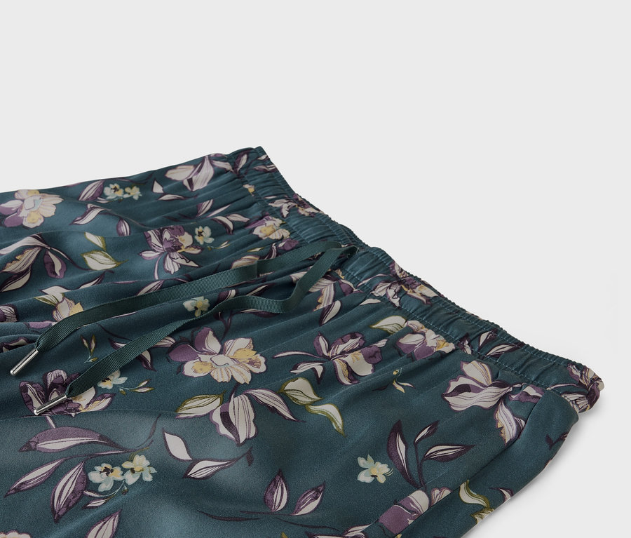 Gros plan sur un pantalon vert émeraude à motifs floraux avec une taille élastique et un cordon de serrage.