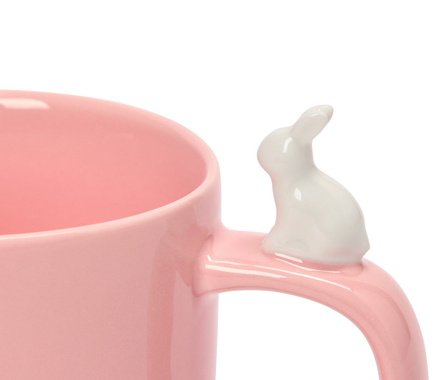 Gros plan d'une tasse rose avec un lapin blanc sur la poignée.