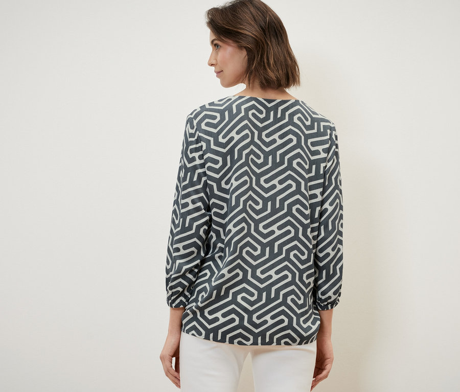 Une femme, de dos, porte une blouse aspect froissé et un pantalon blanc.