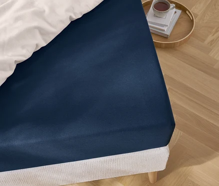 Gros plan d'un drap-housse bleu sur un lit avec une literie blanche et un plateau avec des livres et une tasse.