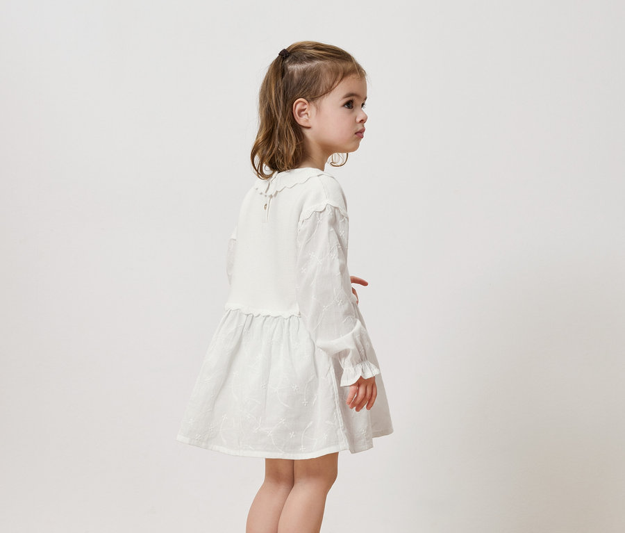 Fillette portant une robe blanche à manches longues et à volants.