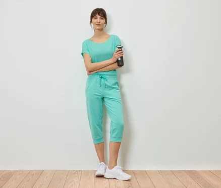 Femme portant un t-shirt menthe et un pantacourt, debout, les bras croisés, tenant une bouteille d'eau.