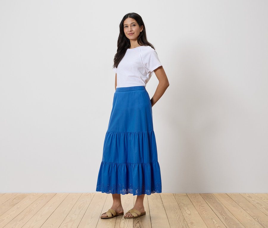 Une femme debout portant un t-shirt blanc et une jupe bleue.