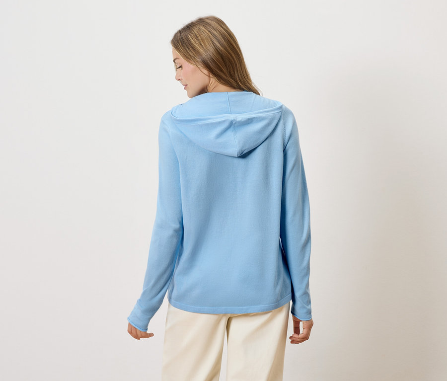 Vue de dos d'une femme blonde portant un sweat à capuche bleu clair et un pantalon beige.