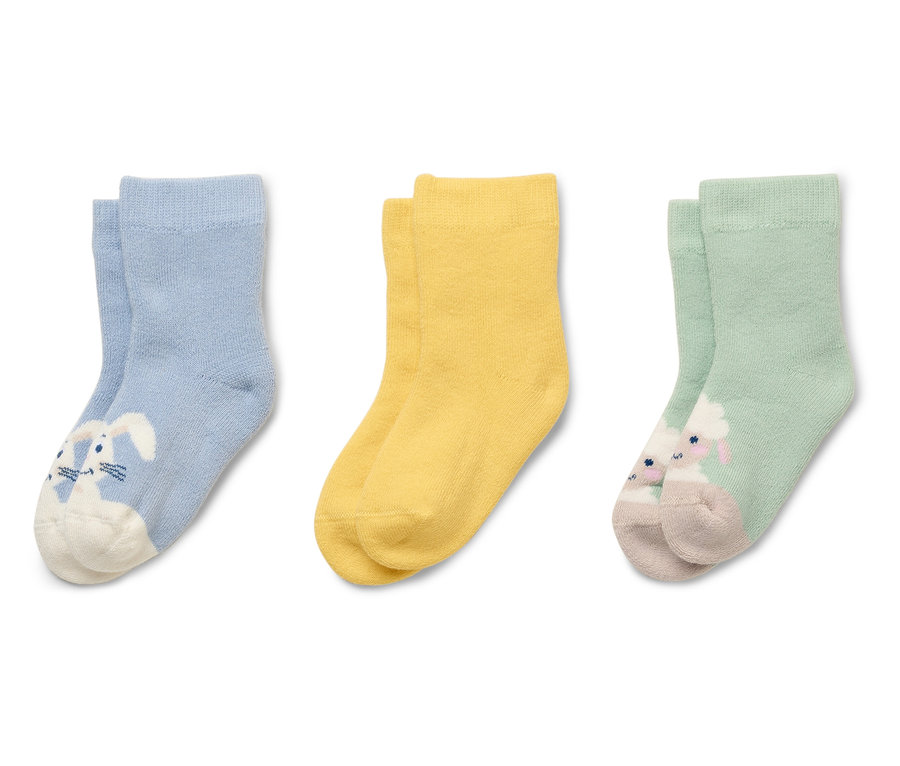 Trois paires de chaussettes pour enfants, bleu clair avec un lapin, jaunes et vert clair avec un mouton, sont disposées côte à côte.