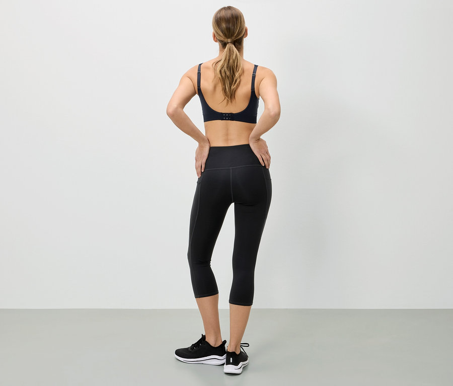 Femme vue de dos portant un soutien-gorge de sport, un legging noir et des baskets, les mains sur les hanches.