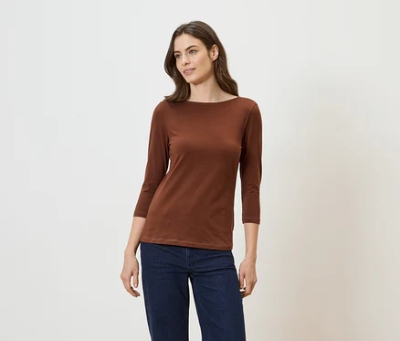 Femme portant un t-shirt marron à manches longues et un jean sur fond clair.