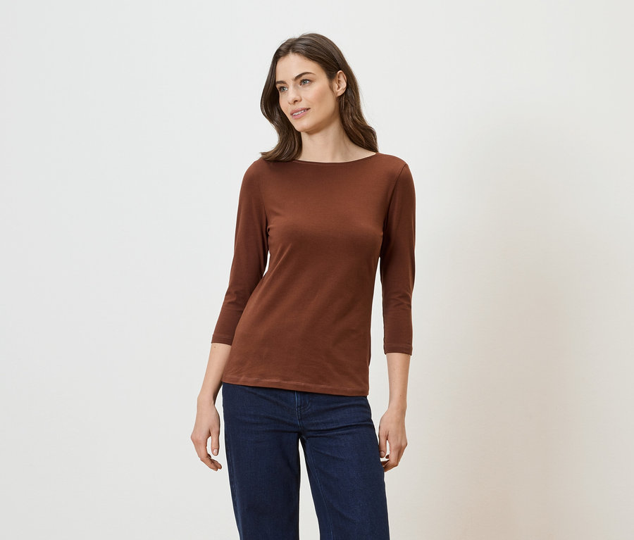 Femme portant un t-shirt marron à manches longues et un jean sur fond clair.