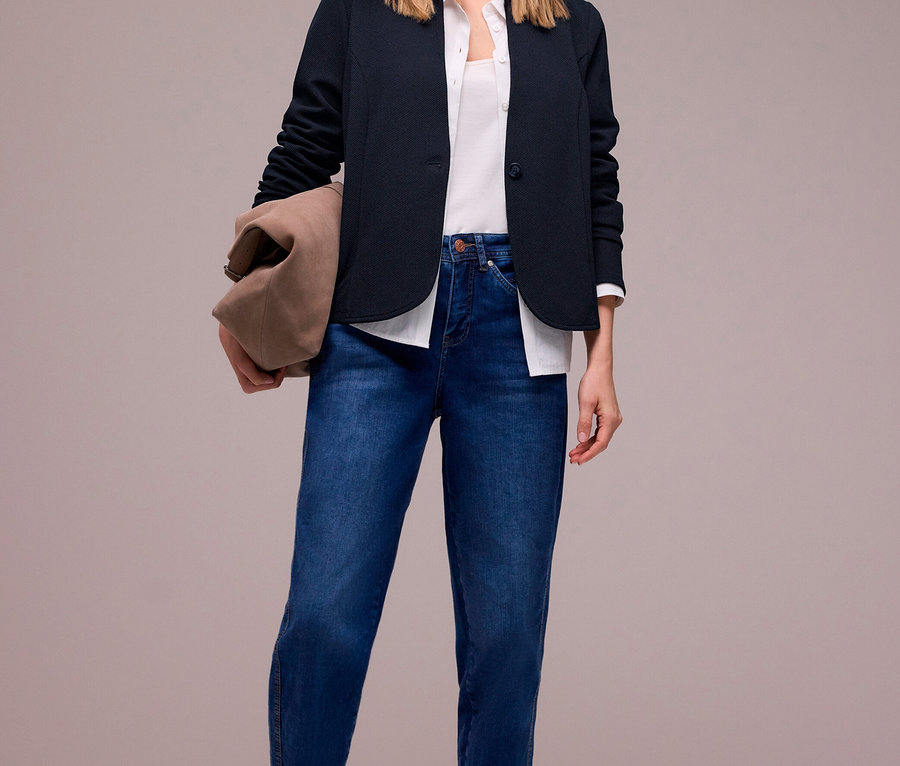Femme souriante portant un blazer en jersey Street One bleu foncé, un haut blanc, un jean bleu et des ballerines taupe, tenant un sac marron.