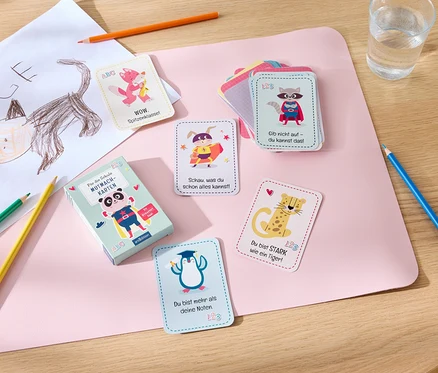 Sur une table sont disposés des cartes de motivation, des crayons de couleur, un verre d'eau et un dessin d'enfant.