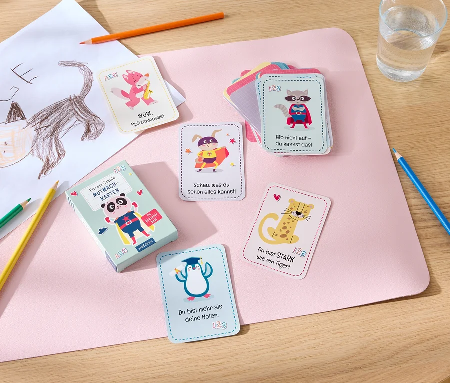 Sur une table sont disposés des cartes de motivation, des crayons de couleur, un verre d'eau et un dessin d'enfant.