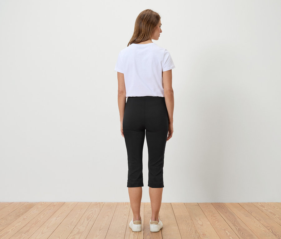 Vue de dos d'une femme aux cheveux bruns portant un t-shirt blanc, un pantacourt noir et des baskets blanches.