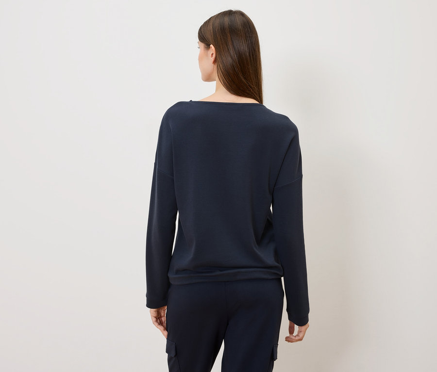 Vue de dos d'une femme aux longs cheveux bruns portant un pull et un pantalon bleu marine.