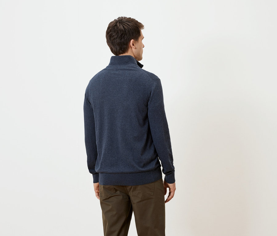 Homme vu de dos portant un pull bleu marine et un pantalon marron sur fond blanc.