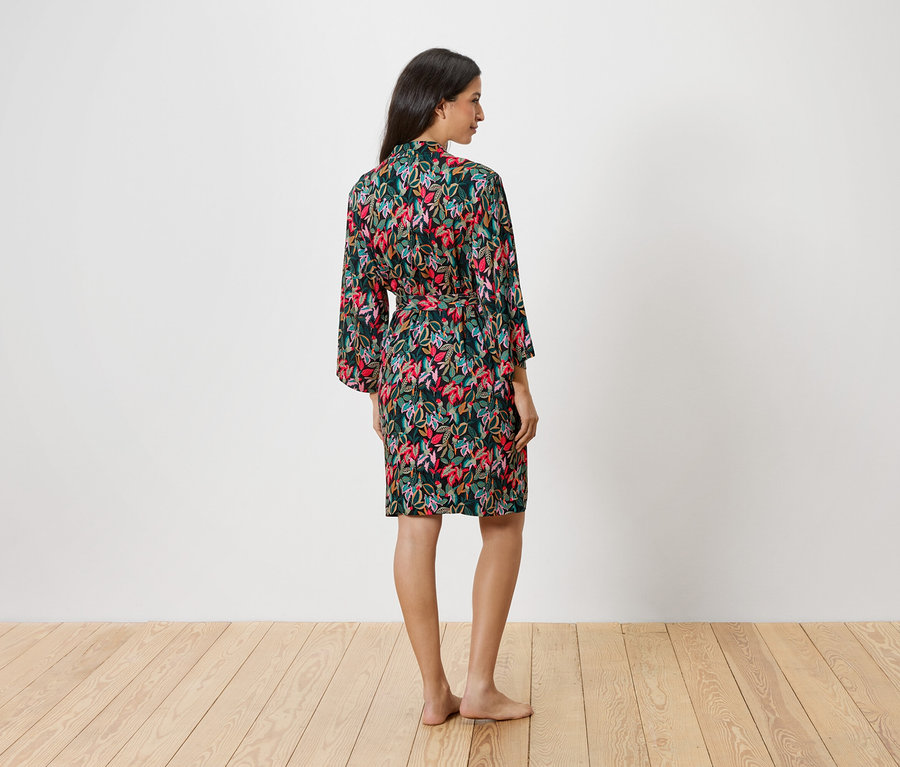 Femme de dos portant un peignoir floral avec ceinture sur fond blanc.