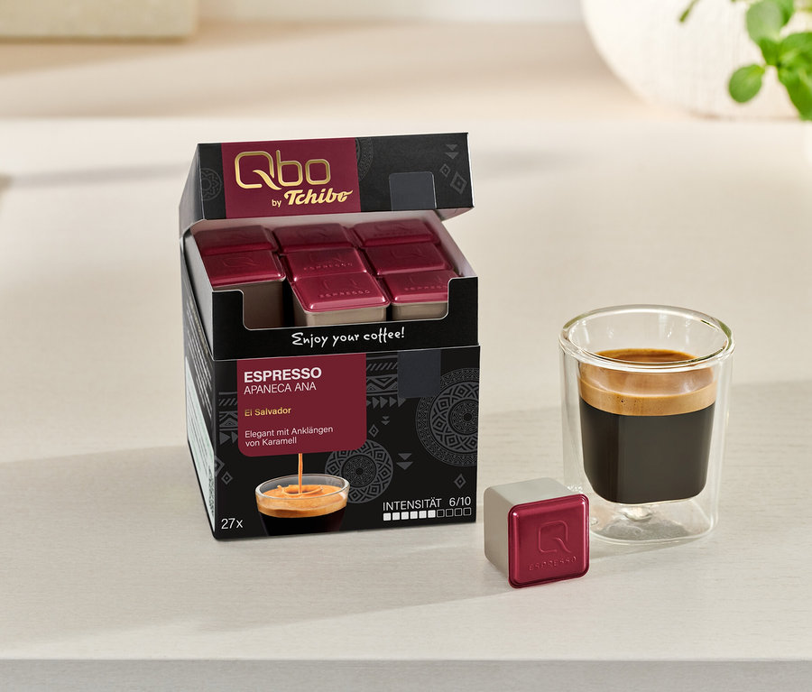 Une boîte ouverte de Qbo Espresso APANECA ANA – 27 capsules à côté d'un verre à espresso et d'une capsule individuelle.